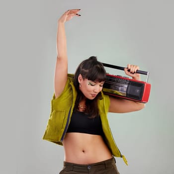 Dance, trendy and woman with a radio for music isolated on a grey studio background. Party, fashion and dancing girl holding a cassette stereo listening to audio, boombox record and track with rhythm.