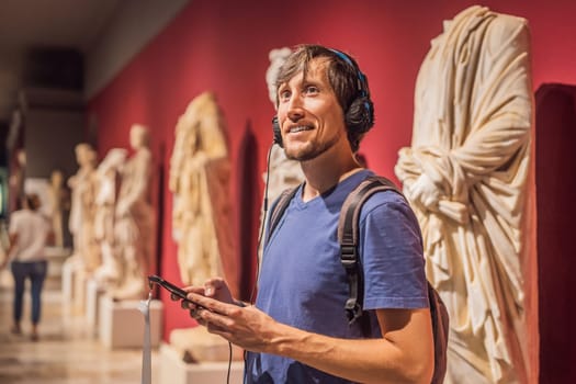Portrait of contemporary man looking at sculptures and listening to audio guide at museum exhibition