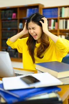 Stressed female student sitting in front of the laptop, having serious computer problem or feeling tired of studying for college exam