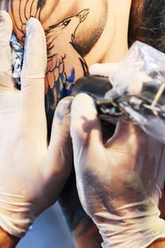 Hands, arm and tattoo gun of artist with blue color ink for permanent bird illustration or precision tool. Closeup of graphic designer applying detail to arms for body art, coloring or drawing
