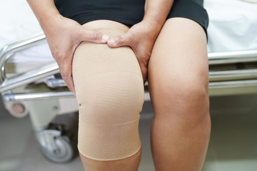 Asian senior woman wearing elastic support knee brace for reduce pain.