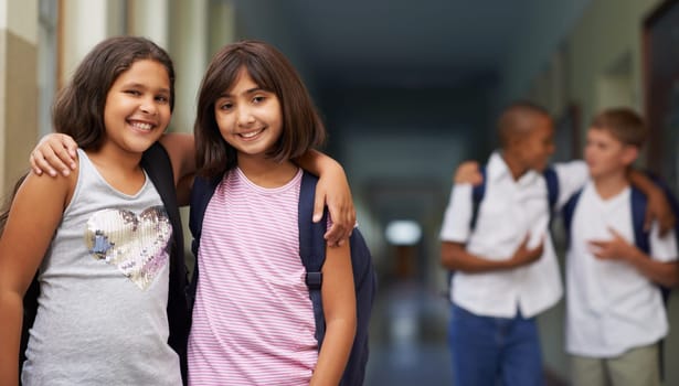 Back to school. Two school girls standing with their arms around each others shoulders in the hallway.