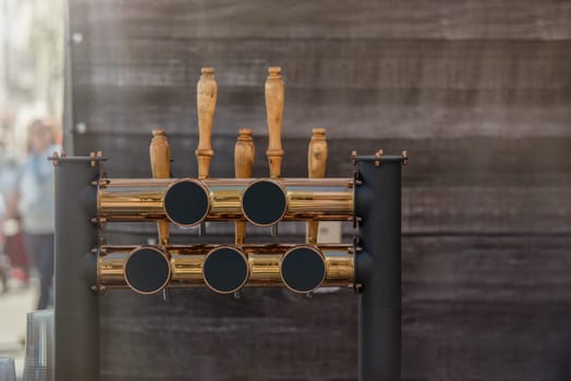 Pouring beer in a bar, mockup for inserting your advertisement. Bronze shiny tap for pouring craft beer on a wooden background, with copy space.