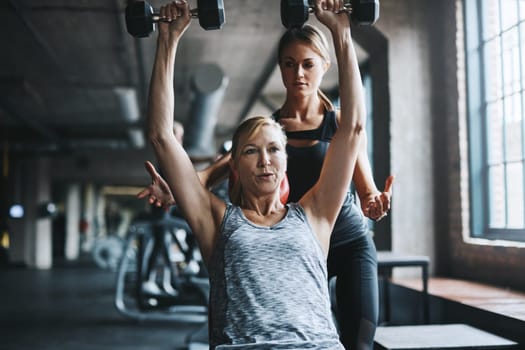 You earn your body, so work for it. a mature woman lifting weights with a female instructor at the gym.