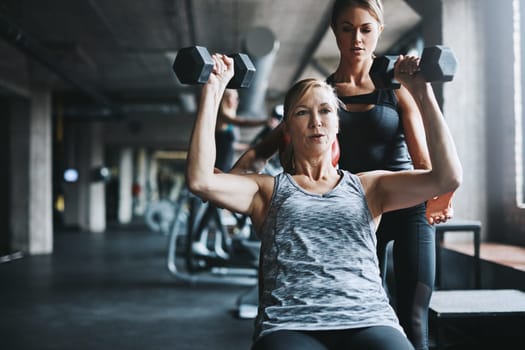 The body you want takes discipline. a mature woman lifting weights with a female instructor at the gym.