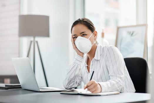 When the unexpected happens, its time to rework the plan. a masked young businesswoman looking unhappy while working at her desk in a modern office.