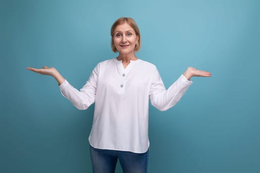 blonde 50s woman in a white blouse in menopause spreads her arms to the sides on a studio background