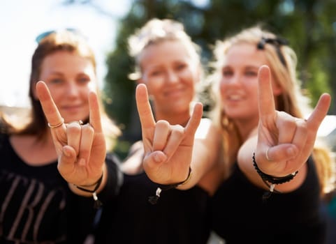 Keep on rocking. Three young girls giving you a rock and roll sign at a music festival.
