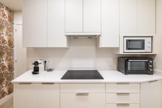 Frontal shot of a white kitchen unit with functional appliances and a convection hob. The concept of convenience and simplicity in interior design for young families