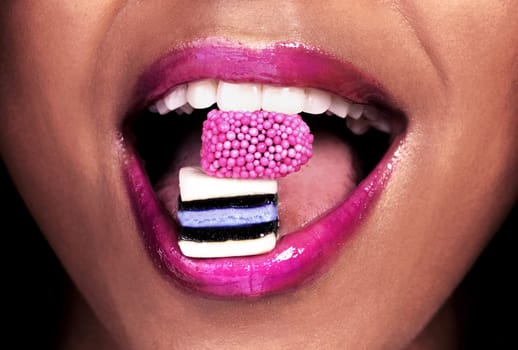 She is as bold as her lipstick. an unrecognizable woman posing with licorice sweets in her mouth.