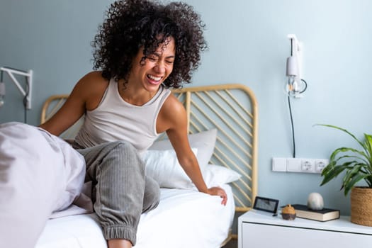 Happy young multiracial latina woman getting out of bed in the morning laughing. Happiness.