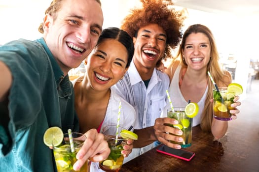 Group of multiracial friends taking selfie together at beach bar looking at camera having mojito cocktails. Happy friends having fun at summertime. Summertime lifestyle concept.