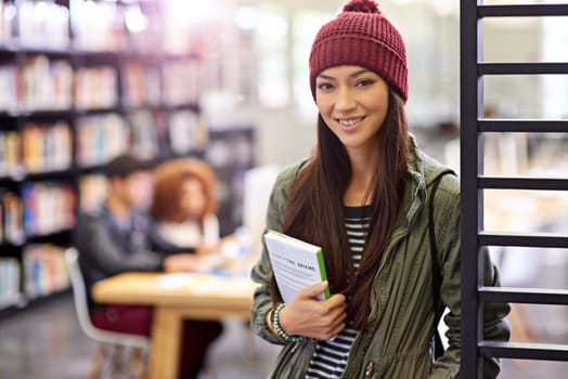 Woman in portrait, student in library with book and study for exam with smile on university campus. Education, learning and academic development with female person holding textbook for knowledge