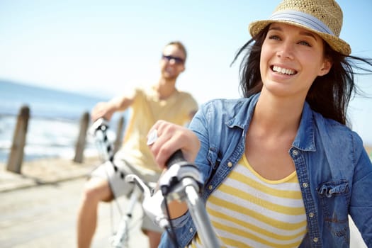 Bike, cycling and couple with a travel woman on summer vacation or holiday riding on the promenade by the beach. Freedom, date and romance with a girlfriend outdoor for a ride on the coast.