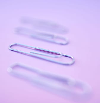 Paperclip, filing and organization for documenting or attachment in studio on a purple background. Business, office and stationery with a metal clip for file or storage purposed on a color surface