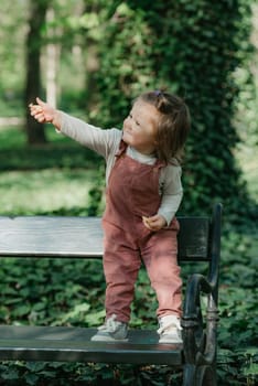 A female toddler is on the garden bench in the park.