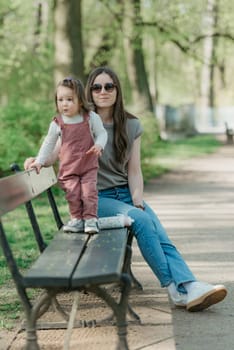 A female toddler in velvet overall is on the bench with her mother.