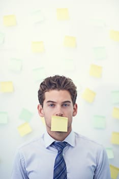 Its all sticky notes and no verbal communication. a young businessman with a sticky note over his mouth.