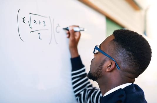 Solving the equation. a young man writing on a whiteboard in a classroom.