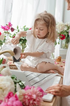A little blonde girl on a kitchen countertop decorated with peonies. Spring atmosphere.