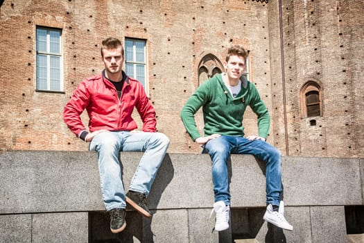 Two young men sitting on low wall in urban setting