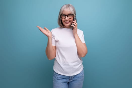 gray-haired 60s woman masters smartphone gadget on bright studio background