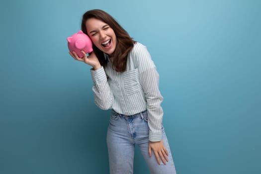 cute 20s brunette lady in shirt and jeans saved up her money for a dream in a piggy bank