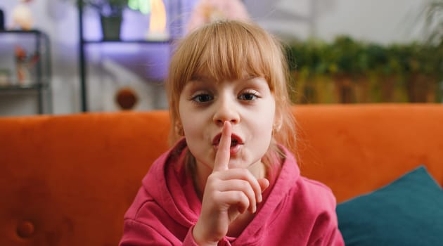 Child kid girl presses finger to lips makes silence hush sign do not tells gossip secret, quiet