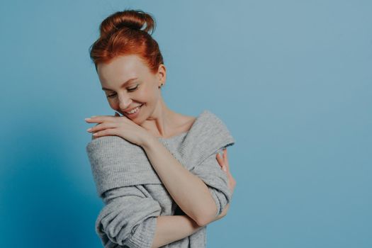 Young beautiful romantic red-haired woman wearing knitted sweater embracing herself with pleasure