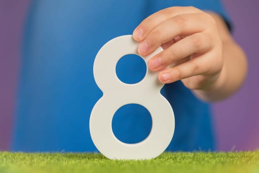Number 8 in hand. A hand holds a white number eight on a purple background, eight percent per annum. The concept of international women's day on March 8. Advertising banner or greeting card.