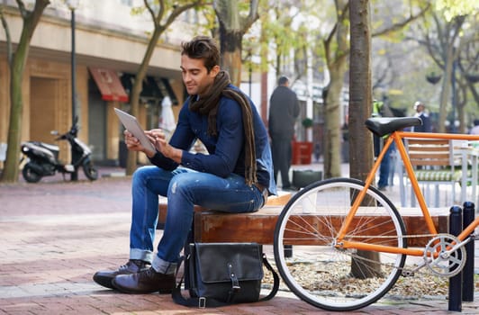 Relaxed city life moments. Shot of a man using his tablet while taking a break in the city with his bicycle beside him.