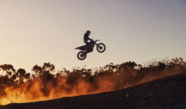 Racing against the sunset. a motocross rider going over a jump during a race.
