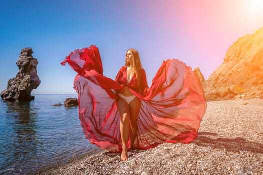 woman sea red dress Happy woman in a flying red dress and with long hair, stands on the seashore.