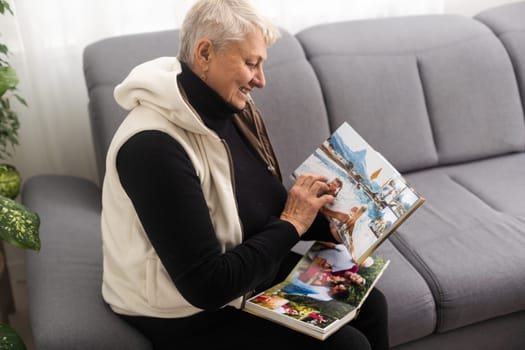 An elderly woman with nostalgia looks at old photos in a photo album or photobook - The concept of family and life values and loneliness in old age.