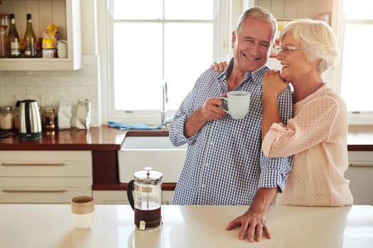 Hug, coffee or happy old couple in kitchen at home bonding or enjoying quality morning time together. Embrace, retirement or senior man talking, relaxing or drinking tea with a funny elderly woman