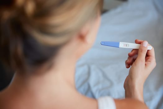 Does anyone else hear mommy bells. High angle shot of an unrecognizable young woman holding a pregnancy test in her bedroom at home.