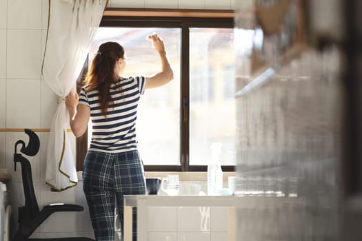 Adult woman housewife washing a window in the kitchen