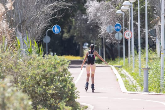A woman rides roller skates in the park - signs indicating the path for a bicycle and a parent with a child