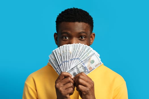 Black guy holding money cash over his face, blue background