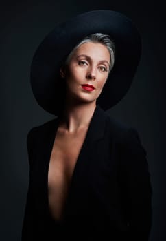 She has class, elegance and style. Studio portrait of a beautiful mature woman wearing a hat and posing against a dark background.