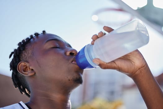 Water, hydration and healthy lifestyle of a sporty black man drinking water from a bottle, enjoying a refreshing drink. African athlete restore electrolytes while being active and exercise outside