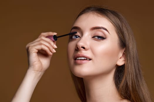 young woman applying black mascara on long thick eyelashes