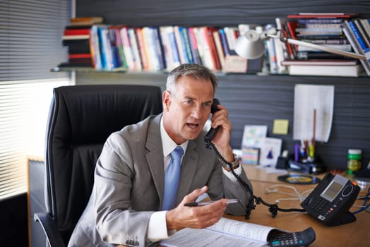 That is unacceptable. a mature businessman looking displeased while talking on the phone in his office.