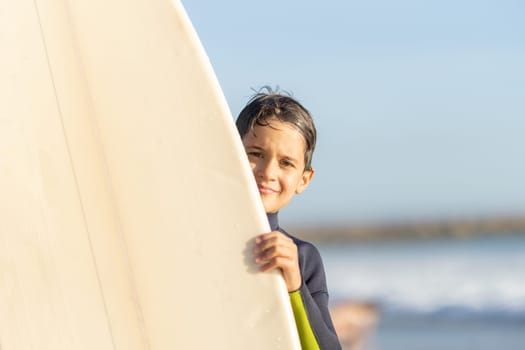 Little boy peeking out from behind a surfboard