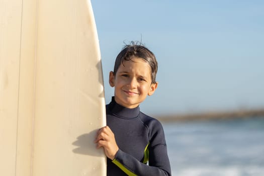 Smiling little boy peeking out from behind a surfboard