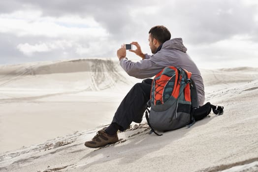 Framing nature. a handsome male hiker sitting on the sand dunes and taking a photograph of the scenery.