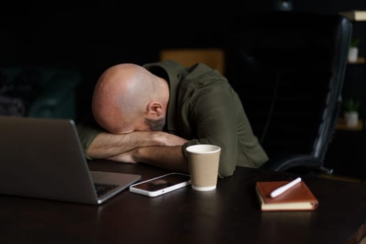 Tired mid-aged worker sleeping with head resting on table near laptop. Concept of age-related changes depicted, highlighting impact of exhaustion and fatigue on individuals as they navigate challenges of work.