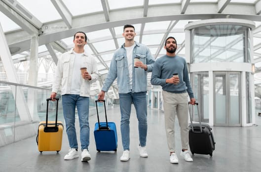 Three Men Walking With Travel Suitcases Holding Coffee In Airport