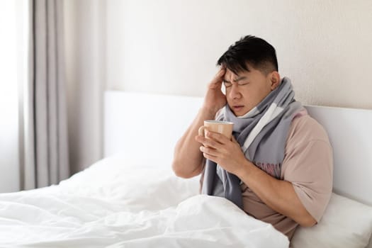 Sick middle aged asian man sitting in bed, got flu