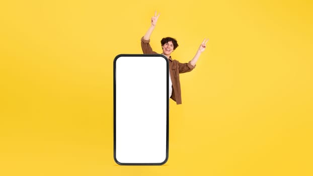 Man Standing Behind Oversized Smartphone's Empty Screen On Yellow Background